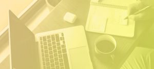 Laptop, coffee mug, and notebook being written in, on a desk.